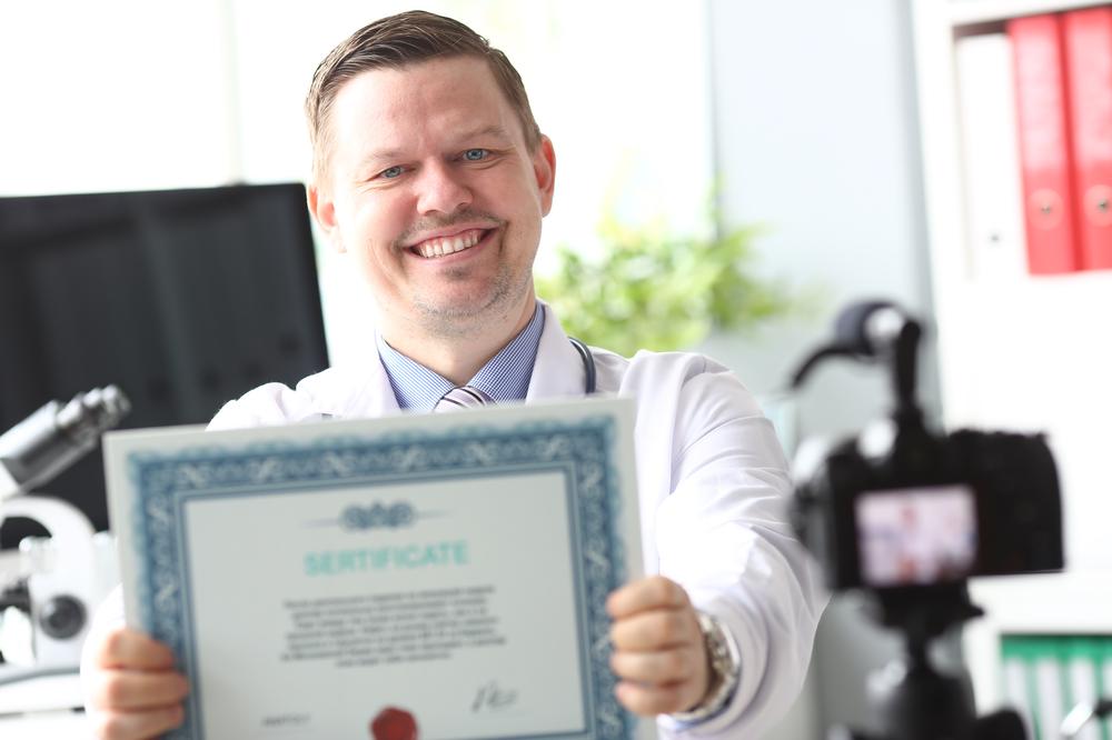 A doctor smiling with a certificate in his hands