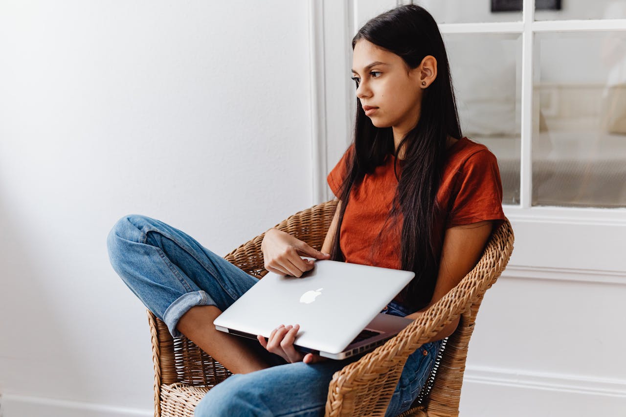 Girl Sitting on a Chair while Holding Her Laptop